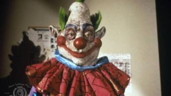 Killer Klowns from Outer Space: Creepy clown with colorful costume and green hair in a dim room.