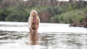 Killing Faith Movie: While holding pink mittens in her teeth, a young girl washes her hands in a pond