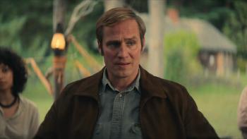 Mr. Car and the Knights Templar movie: A middle aged man in a brown jacket and button down shirt stands with a serious look on his face
