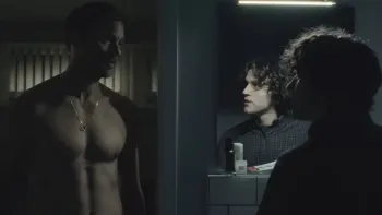 Pillion: A shirtless White man looks at a younger White man who is standing in a bathroom