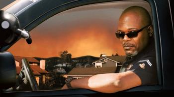 Samuel L. Jackson is driving a police car in uniform, wearing sunglasses. 