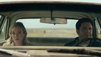LaRoy, Texas: John Magaro drives a car as Megan Stevenson sits in the passenger seat beside him, a desert view behind them
