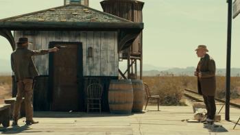 Last Train to Fortune Movie: At a desolate train station, Dooley aims his gun at Cecil, who holds his hands on his lapels