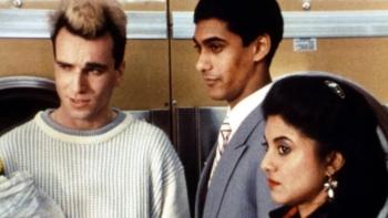 My Beautiful Laundrette: A young White man and a young British Asian man and woman stand together in front of yellow washing machines