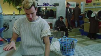 My Beautiful Laundrette: A young White man attends to a washing machine in a laundromat, as other men watch him from across the room