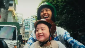 Left-Handed Girl movie: Taiwanese girl, lower center, rides a motorcycle with her mother behind her, top center, both with helmets, down a busy street