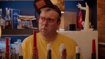 Life Is Sweet: A man wears a yellow top and red baseball cap as he looks confused in front of a row of candles