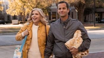 A man and woman smiling and walking, carrying a diaper bag and blanket.