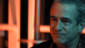 Lights Out Movie: Sage (Dermot Mulroney), apparently seated at some kind of night club, with pink-orange neon lights behind him
