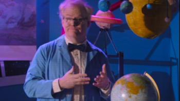 Linoleum Movie: Jim Gaffigan hosting a children's science TV show wearing a blue lab coat in front of a globe 