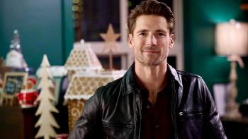 She's Making a List movie: A young White man smiles as he stands in a room with Christmas decorations in the background