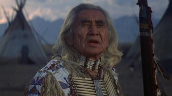 Little Big Man: Chief Dan George stands in front of teepees, the mountains in the background.