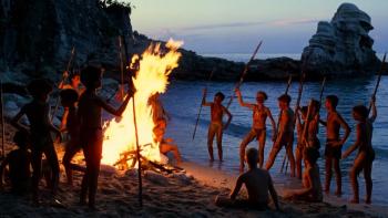 Lord of the Flies movie: Boys sitting and standing around a fire on the beach raise their spears