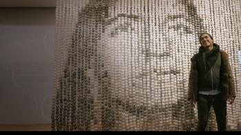 Love and Fury: Native American man on right stands in front of large art piece showing Native American woman's face