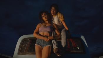 Love Lies Bleeding Movie: Katy O'Brian and Kristen Stewart sit close to each other on  the back of a truck