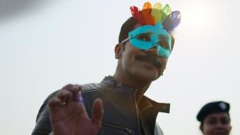 Badhaai Do: An India man wearing a multi-colored face mask smiles and waves. 