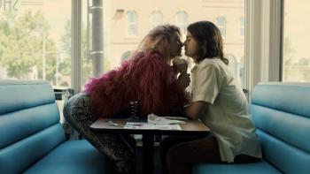 Marmalade: Camila Morrone leans over a table in a diner to kiss Joe Keery, both of them sitting in front of a window