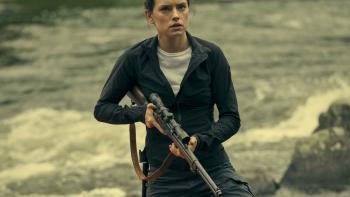 The Marsh King's Daughter Movie: Daisy Ridley holds a rifle at the ready while standing next to a canoe in the nature