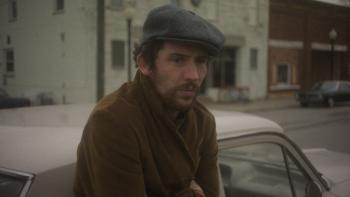 The Mastermind Movie: J.B. (Josh O'Connor) wears a newsboy cap and huddles against the cold