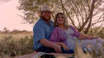 Maternal Instinct movie: Couple sitting on a blanket in a field, smiling at sunset.