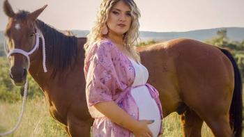 Maternal Instinct movie: Pregnant woman in pink robe standing beside a brown horse in a grassy field.