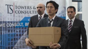 Mayhem: Man stands in office building holding a cardboard box of his belongings, flanked by two security guards