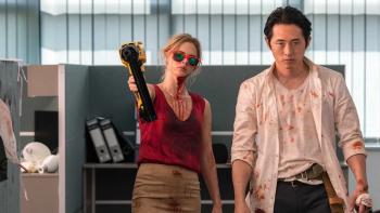 Mayhem: Woman in red holding a weapon, man beside her, both with blood stains in an office setting