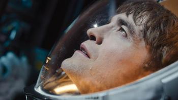 Mickey 17 Movie: Mickey (Robert Pattinson), in a spacesuit, looks upward at something bright, which shines on his face
