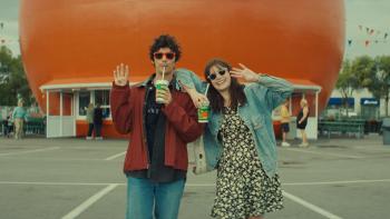 Mile End Kicks movie: Devon Bostick as guitarist Archie and Barbie Ferreira as music critic Grace slurp drinks in front of an orange building