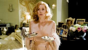 Amy Adams wears a pink dressing gown and holds plates of jewelry, looking scandalized in a fancy British apartment.