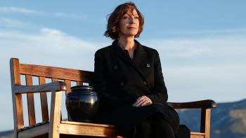 Miss You, Love You: Allison Janney sits on a bench outside in a black coat, next to an urn
