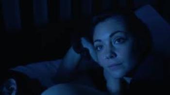 Moon Students: Mexican American woman on right rests head on hand while lying down in dark room
