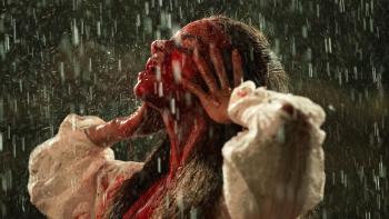 Unwelcome: A woman with blood on her face looks up to the skies as rain falls down on her
