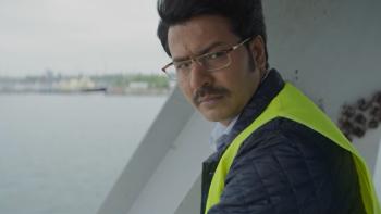 Mrs. Chatterjee vs. Norway: A middle-aged Indian man looks over shoulder wearing yellow hi-vis vest with water and steel girder in background