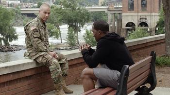 My Brother's Keeper Movie: A White soldier in fatigues sits on a ledge at the waterfront, talking to a Black man sitting on a bench