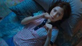 My Dearest Assassin: Woman lying on a bed, wearing a striped shirt, looking up thoughtfully.