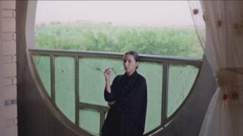 Naga movie: Saudi woman in black shawl center stands on balcony smoking a cigarette