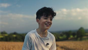 Name Me Lawand: A young boy smiles as he sits in a quiet field