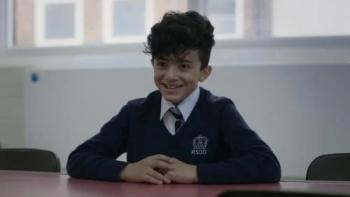 Name Me Lawand: A young boy smiles as he sits at a desk wearing a school uniform
