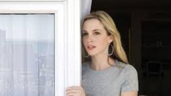 Natalee Holloway movie: Woman in a gray shirt standing by a window, looking outside.