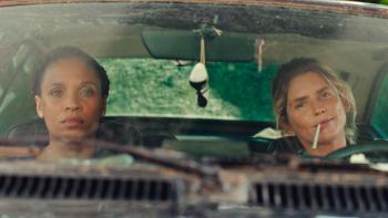 Nice Girls movie: Black French woman left and White French woman with cigarette in mouth right, sit in front of car