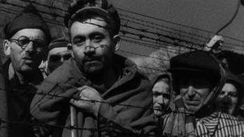 Night and Fog: A group of Jewish people look through a fence of barbed wire in a concentration camp