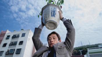 No Other Choice Movie: Seen from below, Man-su hoists a heavy potted plant above his head, as if about to drop it