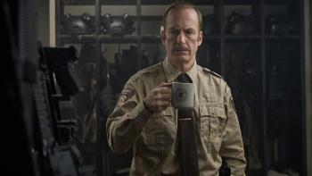 Normal Movie: Ulysses (Bob Odenkirk) holds a cup of coffee and looks around at a well-stocked police station artillery