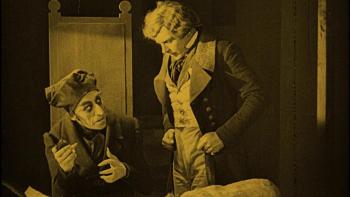 Gustav von Wangenheim leans over a table, as Max Schreck look up from his chair in Nosferatu: A Symphony of Horror