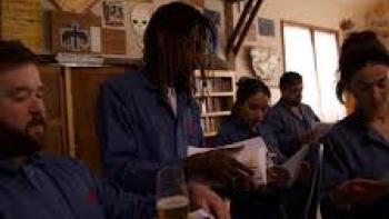 Not an Artist movie: Haley Joel Osment and four other adults wear dark blue jumpsuits hold champagne while each reads from a paper packet in hand
