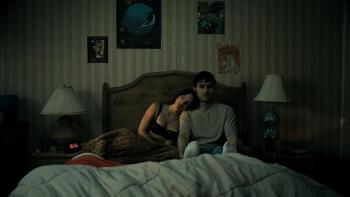 Obsession Movie: On a bed, Nikki leans her head on Bear's shoulder as he sits rigidly against the headboard