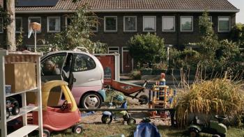 Occupied City Movie: A house with the view blocked by a yard filled with large children's toys and a tiny pink car