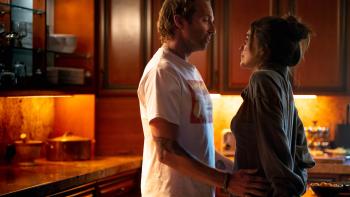 Off the Record movie: Ryan Hansen and Rainey Qualley stand in a kitchen, looking into each other's eyes