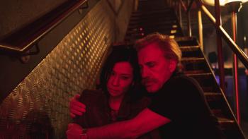 Old Guy movie: Christoph Waltz sits on the stairs with his arms around a dejected Lucy Liu, giving her a comforting hug